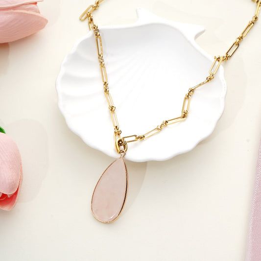 Gold necklace with a Rose Quartz pendant on a white dish with pink flowers in the background