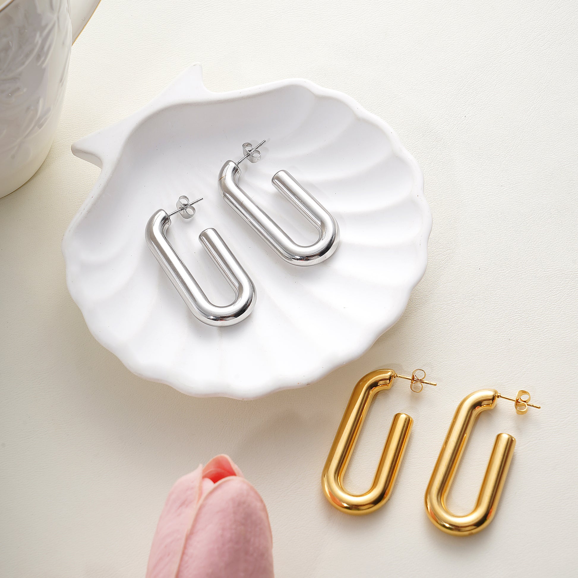 Silver and gold U-shaped earrings on a white dish with a pink flower.