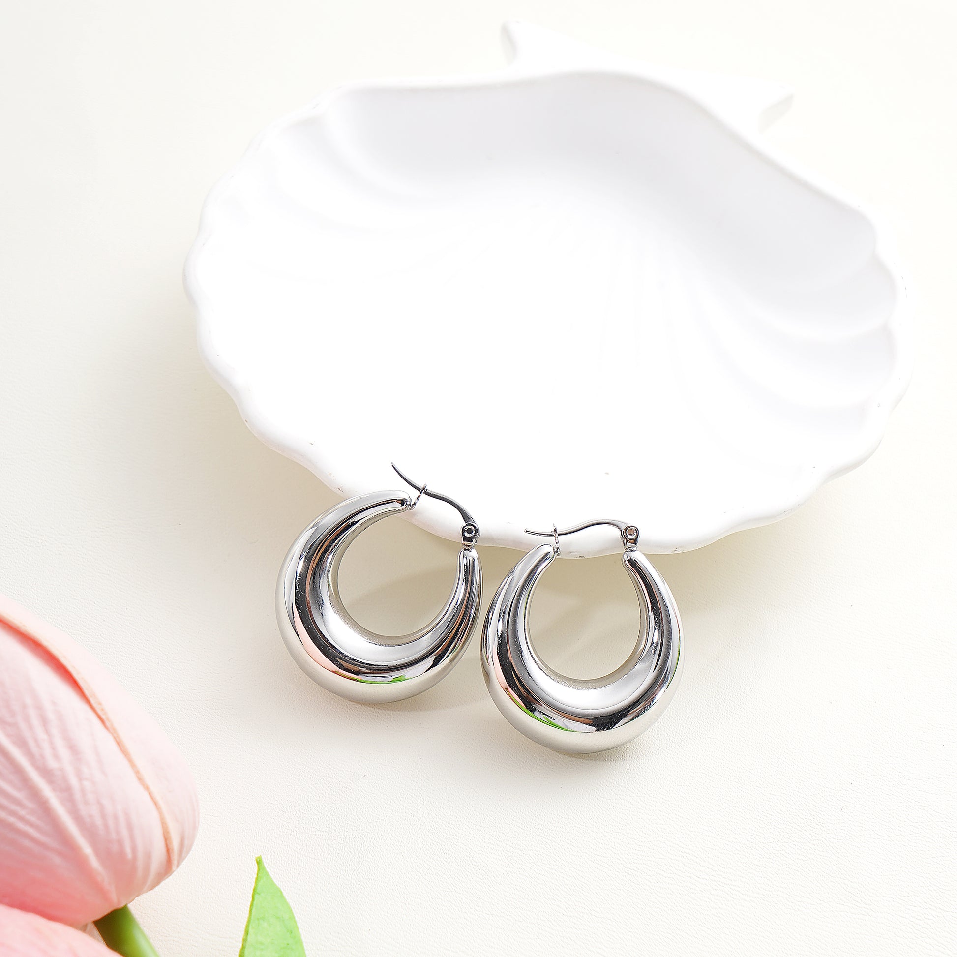 Silver hoop earrings on a white surface with a pink flower in the background