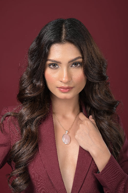 Woman wearing a necklace with a pink Rose Quartz stone against a red background