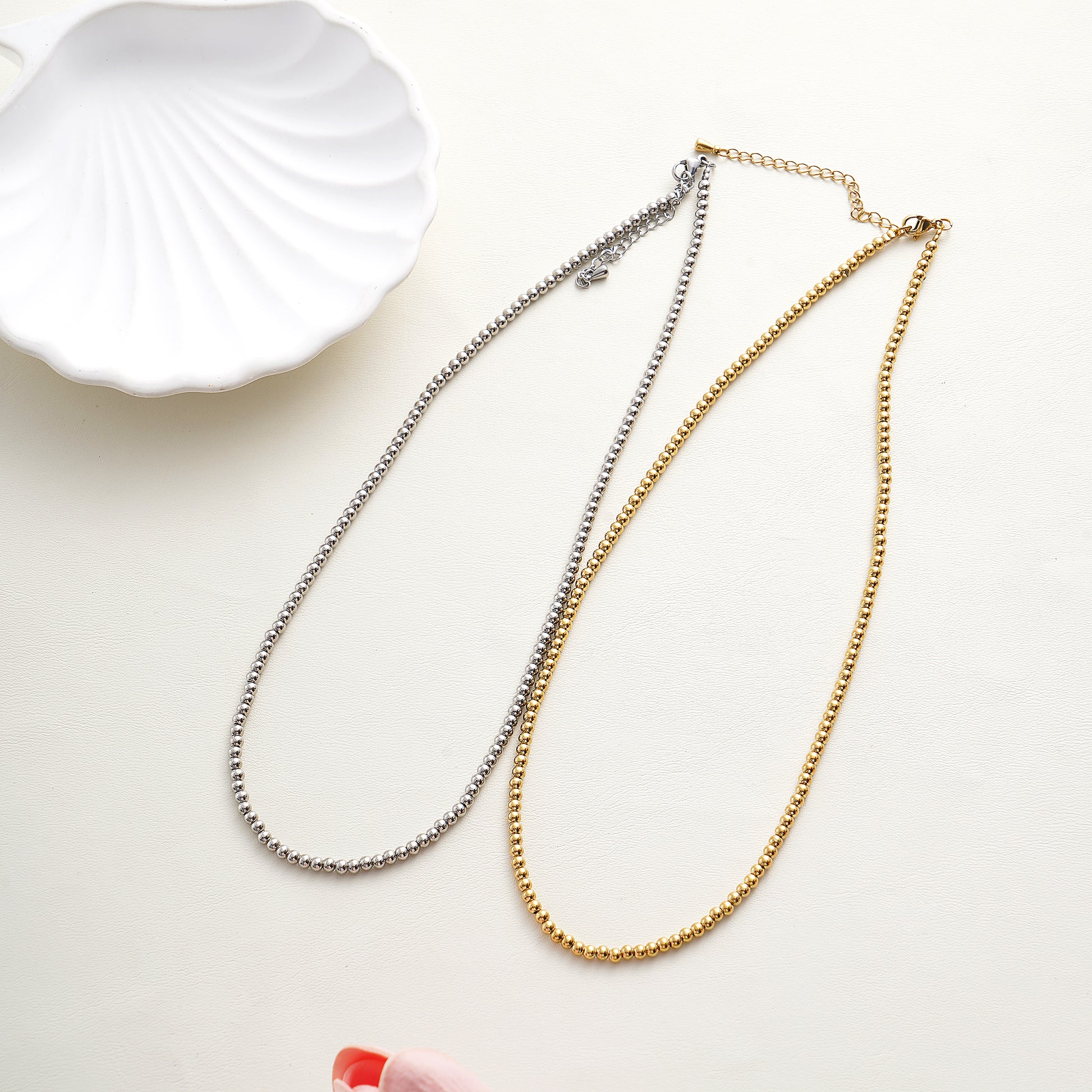 Two gold and silver necklaces on a white surface with a shell in the background.