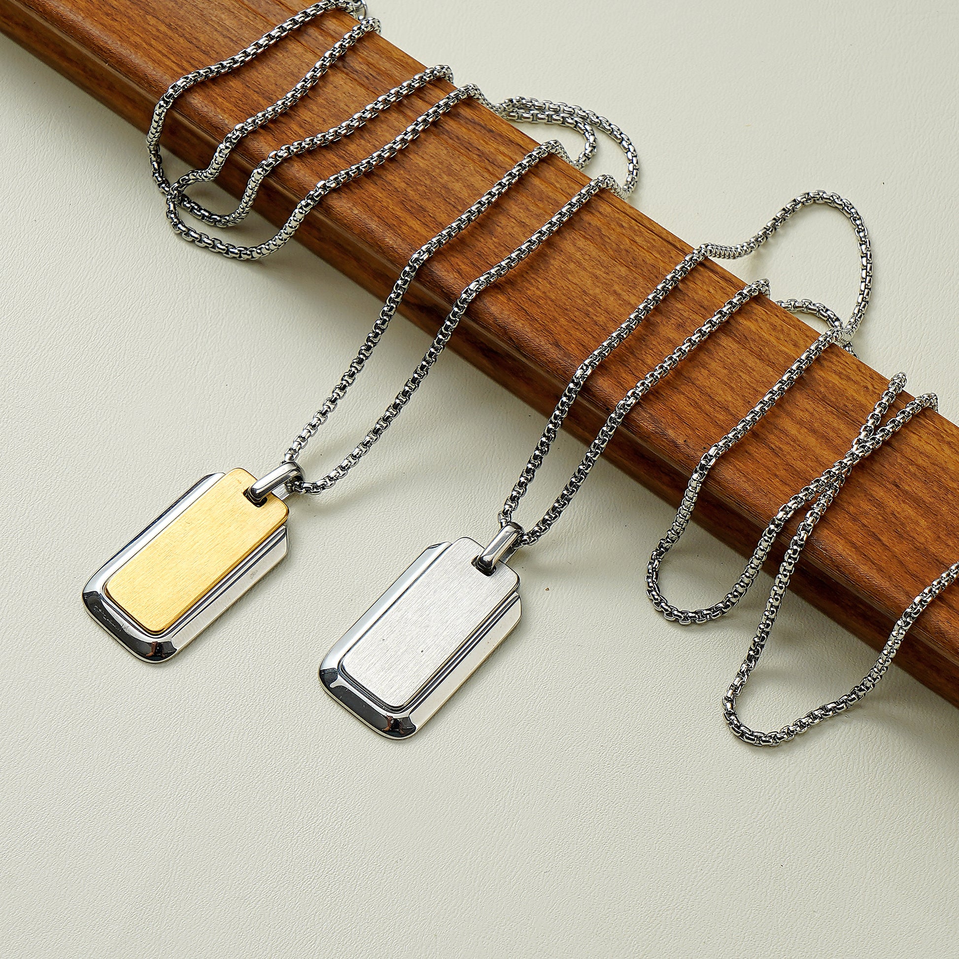Two necklaces with rectangular pendants on a wooden stick.