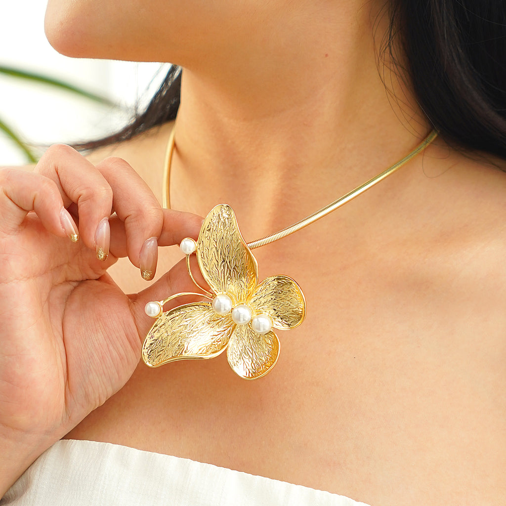 Woman wearing a gold butterfly and pearl collar necklace styled with a square-neck dress