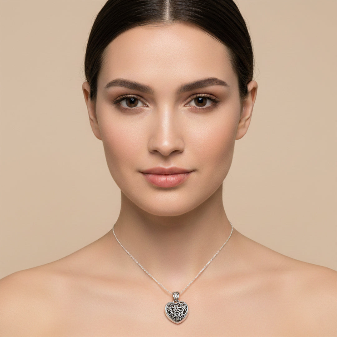 Woman wearing a silver necklace with a heart pendant against a beige background