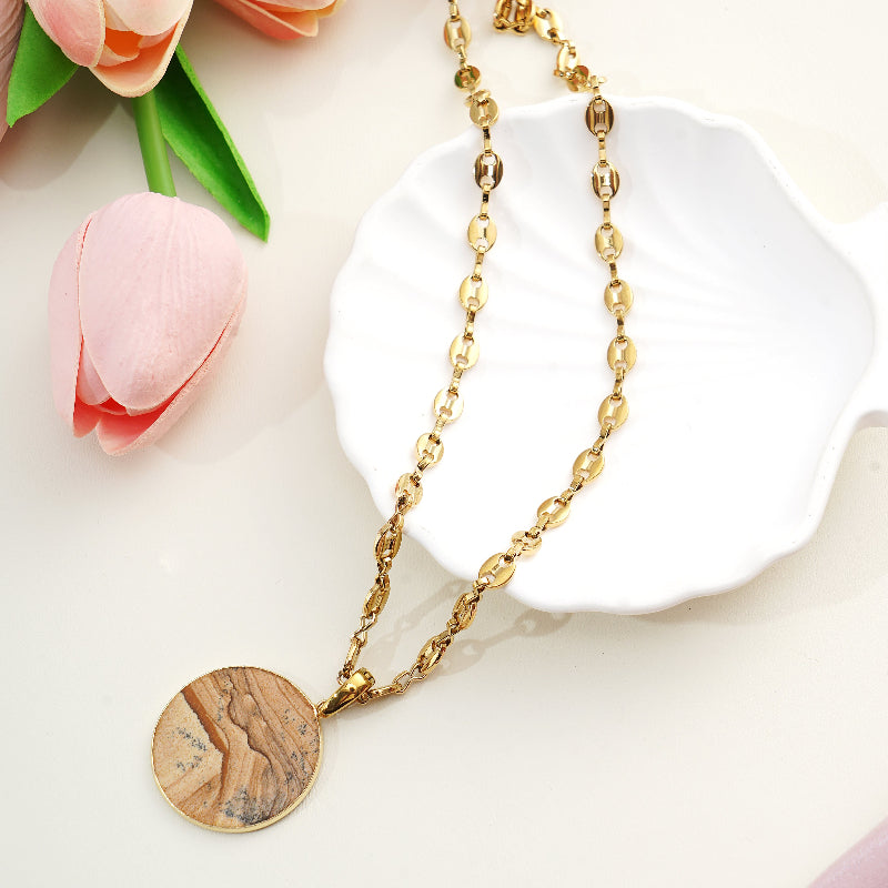 Gold necklace with a circular gemstone pendant on a white surface