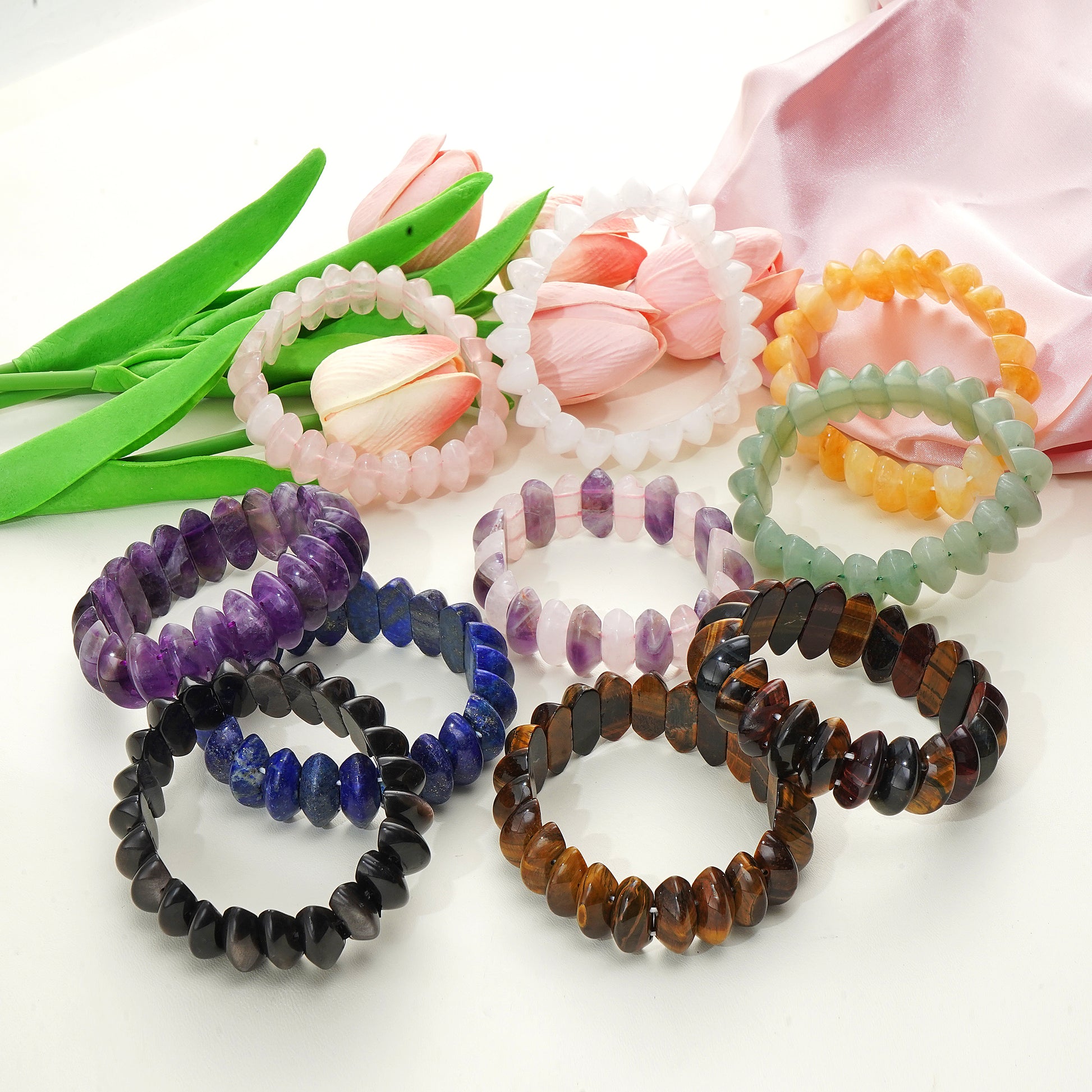 Set of colorful beaded bracelets on a white surface with tulips in the background