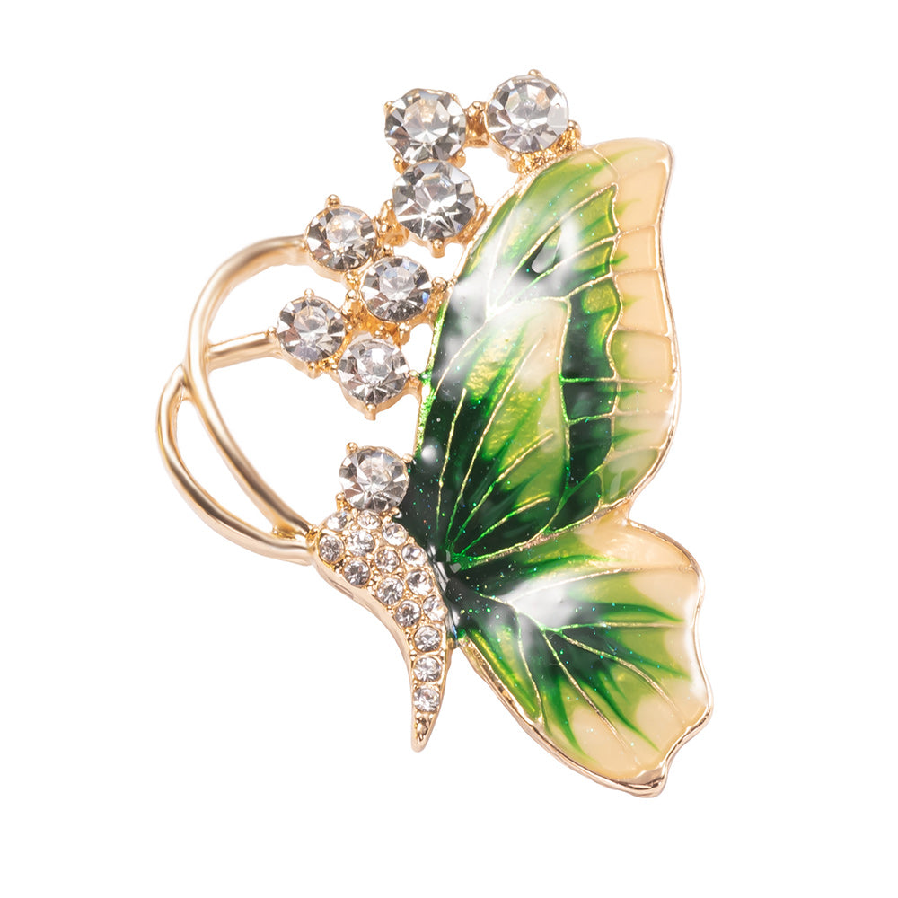 Butterfly-shaped brooch with green wings and crystal accents on a white background