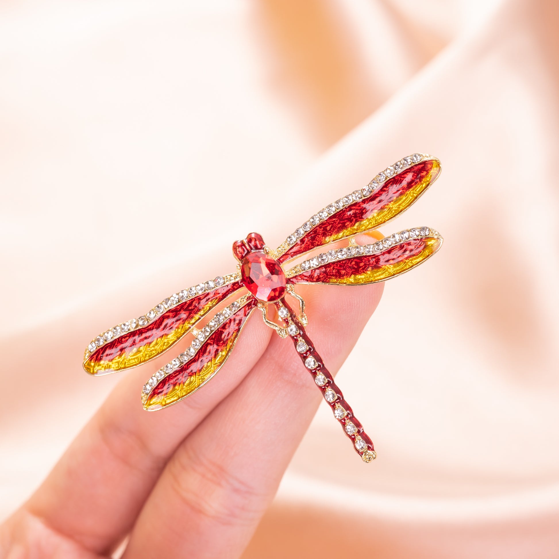 Red and gold dragonfly-shaped brooch on a hand against a soft background