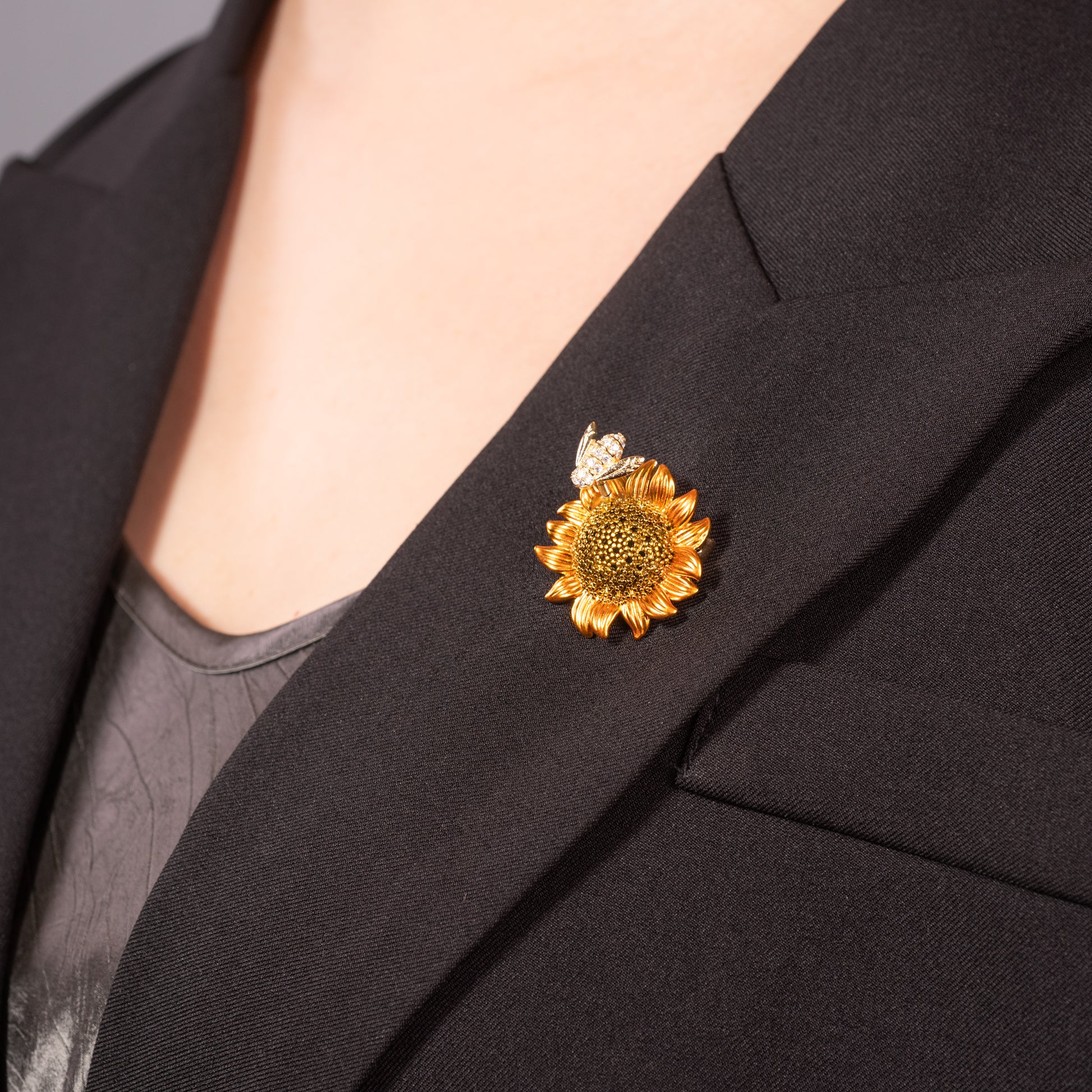 A brooch pin featuring a sunflower with a bee on top, made with cubic zirconia.
