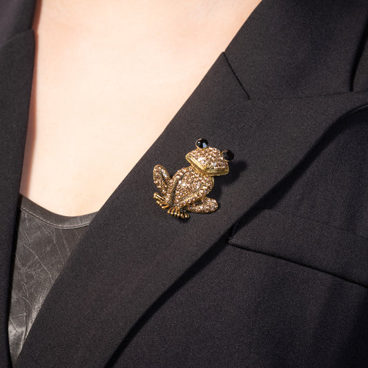 A yellow gold over brass brooch pin featuring a sparkling, champagne crystal-encrusted frog design.