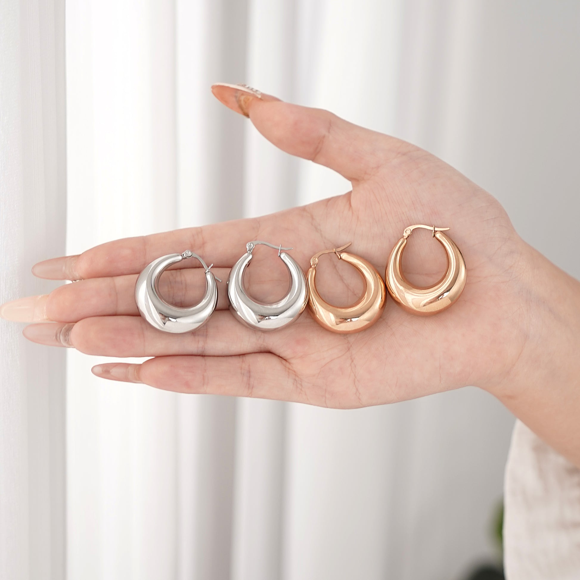 Hand holding four hoop earrings in silver, gold, and rose gold on a white background