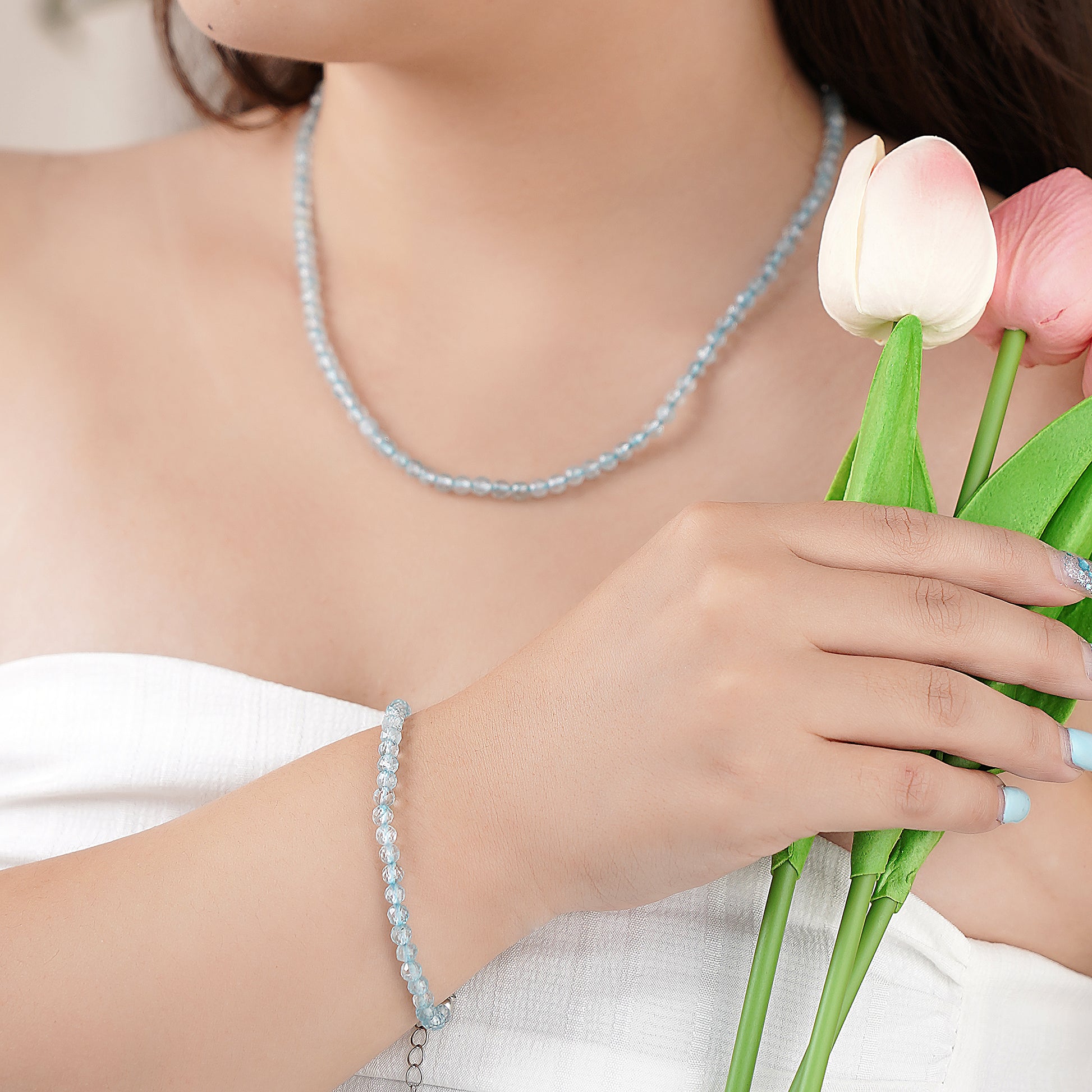Person wearing a light blue beaded necklace and bracelet, holding pink tulips.