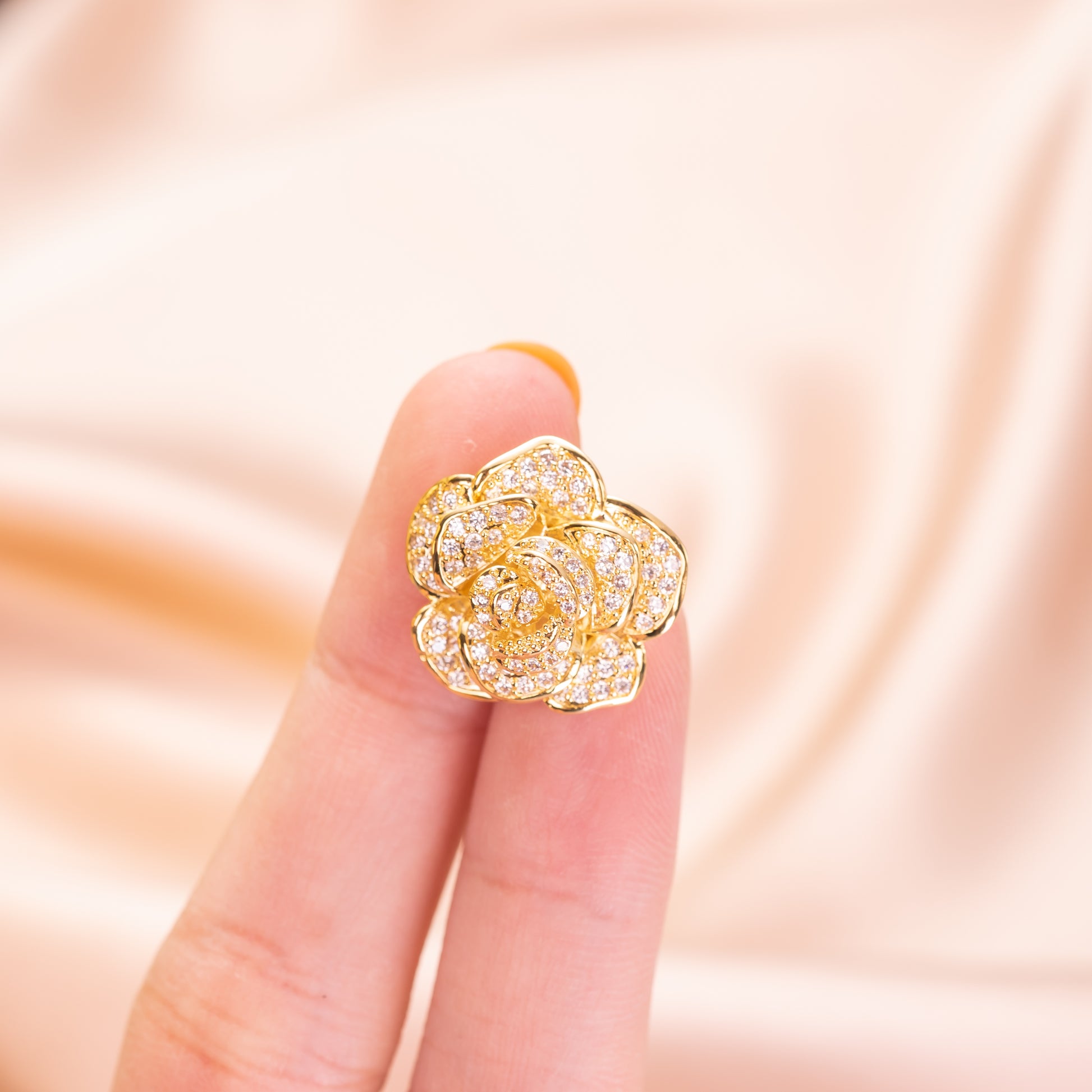 Gold flower-shaped earring on a finger against a soft pink background