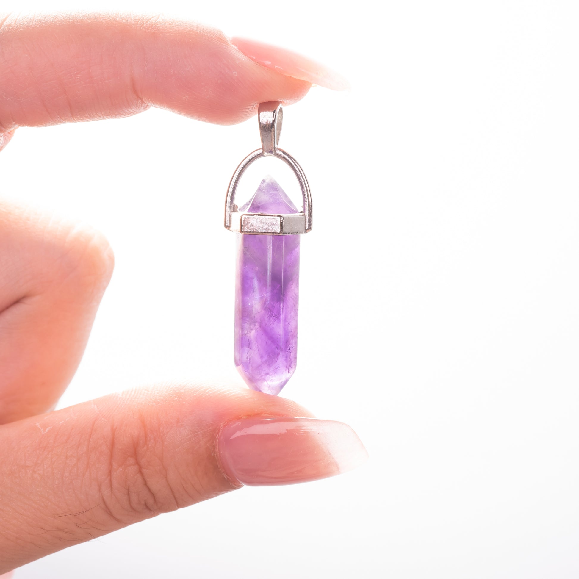 Hand holding a purple crystal pendant against a white background