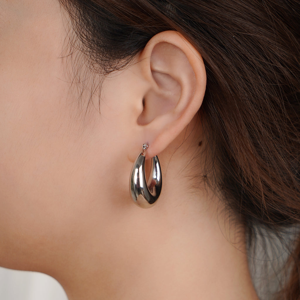 Close-up of an ear wearing a silver hoop earring with a blurred background