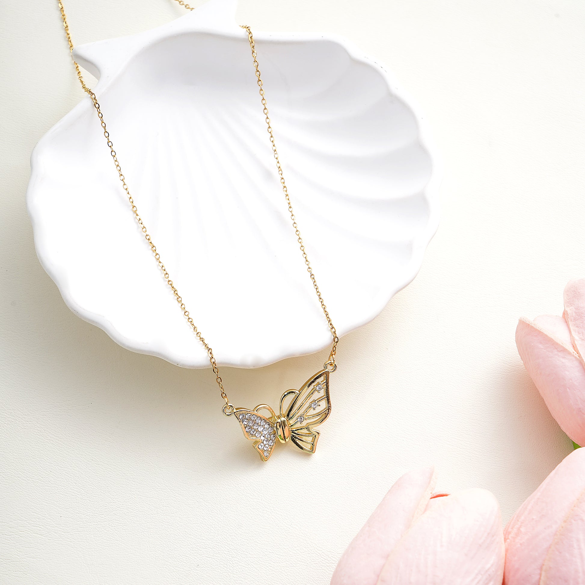 Gold butterfly necklace on a white dish with pink flowers in the background